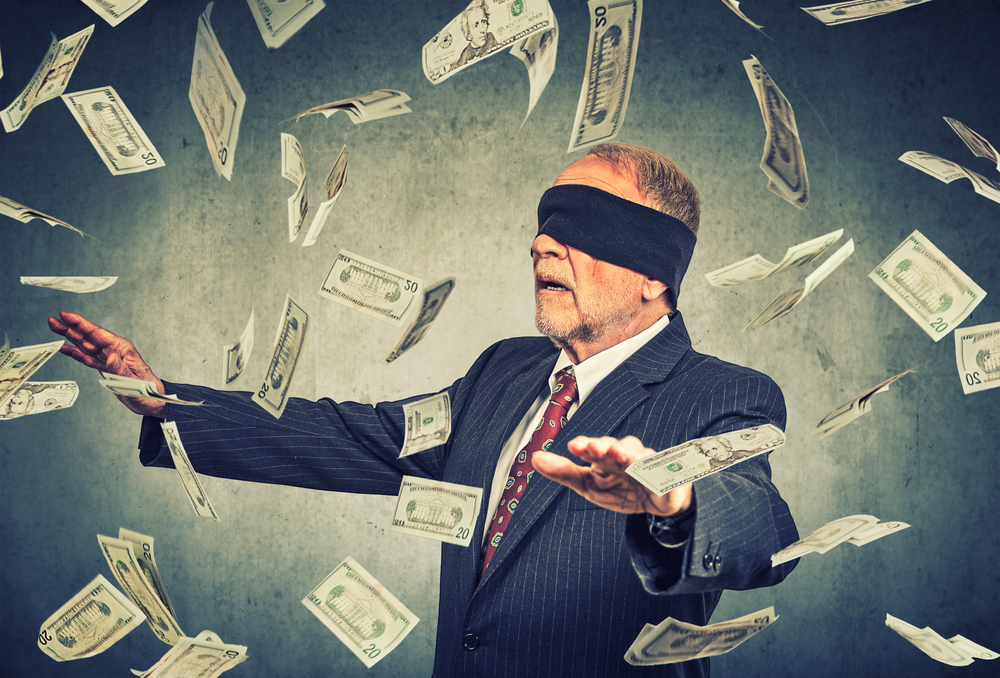 Blindfolded senior businessman trying to catch dollar bills banknotes flying in the air on gray wall background. Financial corporate success or crisis challenge concept Blindfolded senior businessman trying to catch dollar bills banknotes flying in the air on gray wall background. Financial corporate success or crisis challenge concept